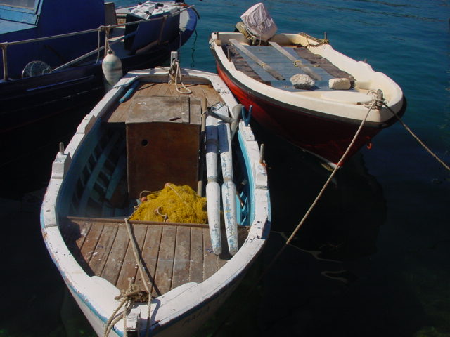 Two small wooden boats are tied to a dock, floating on calm water with fishing equipment on board.