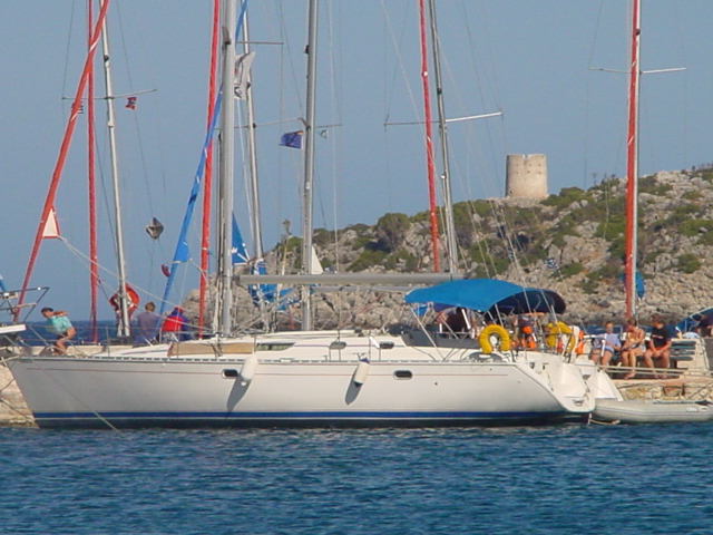 A white sailboat docked at a marina with people gathered on board and along the pier.