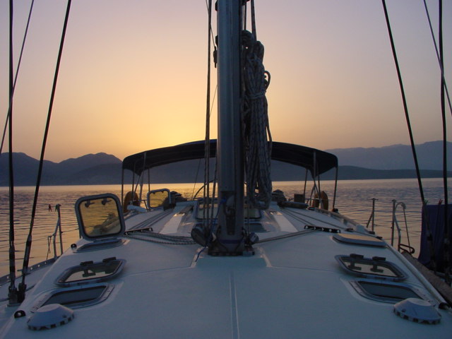 View from a sailboat deck at sunset, with calm water and distant mountains in the background.