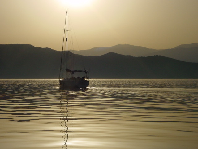 A sailboat floats on calm water with mountains in the background during sunset.