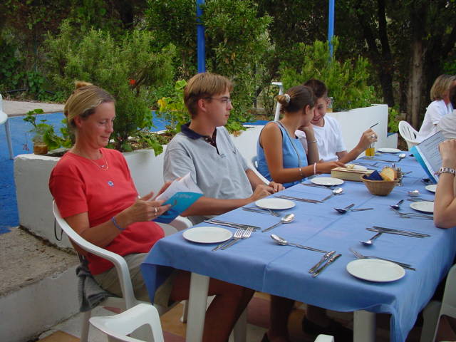 People sit at an outdoor table with blue tablecloths, looking at menus and preparing for a meal.