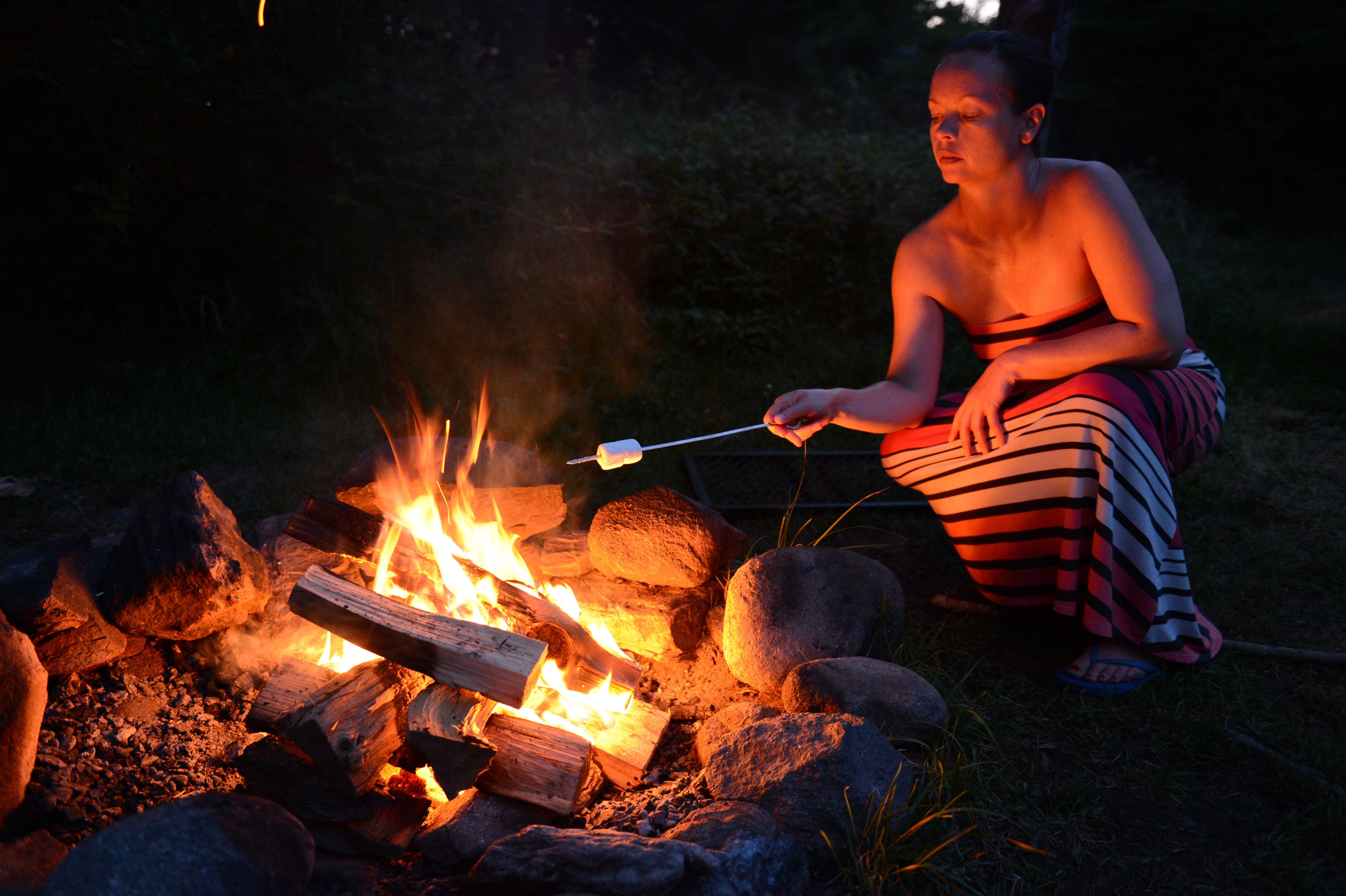A person in a striped dress roasts a marshmallow over a campfire at night.