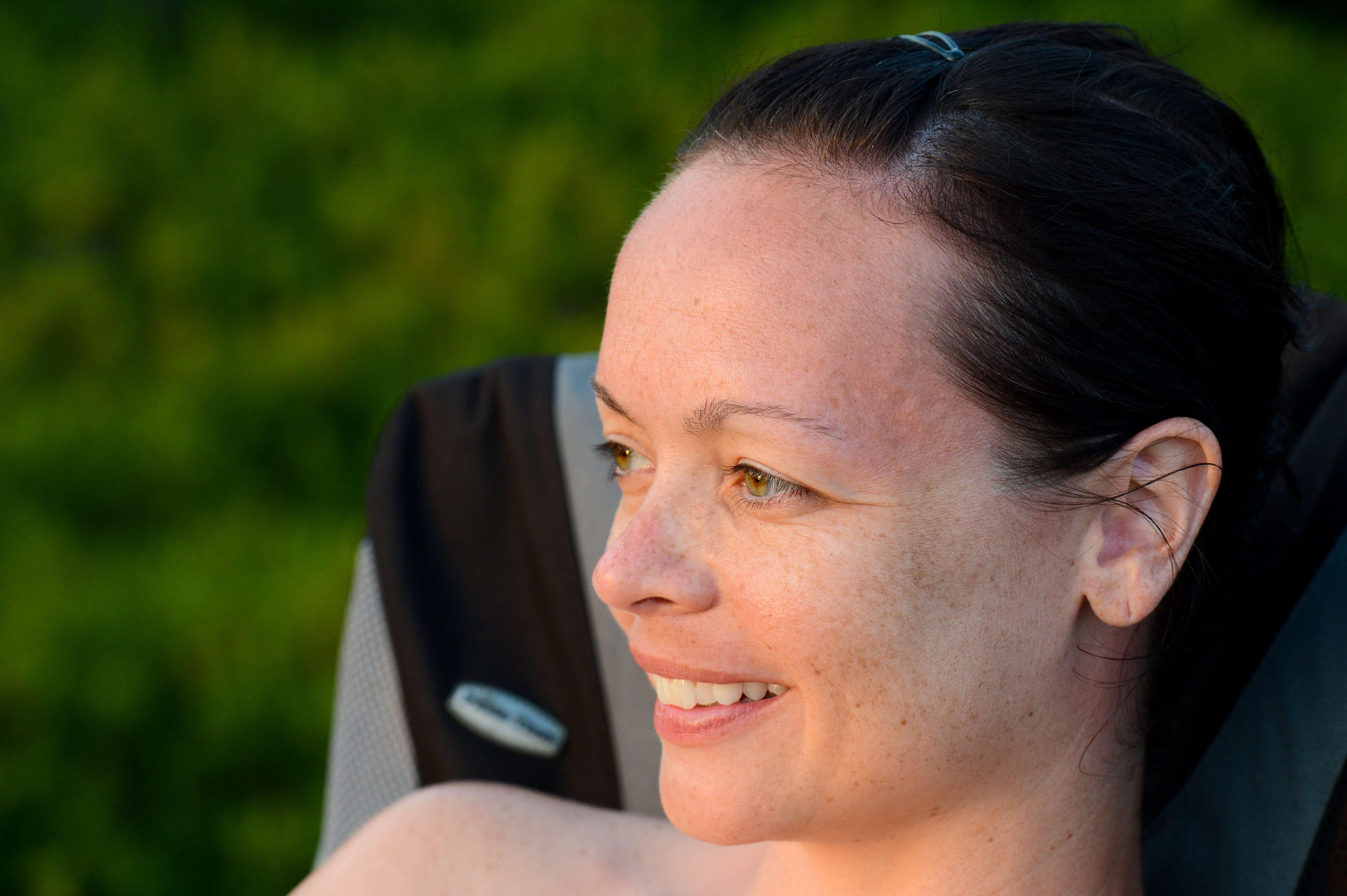 A woman sits in a camping chair, smiling and looking off to the side.