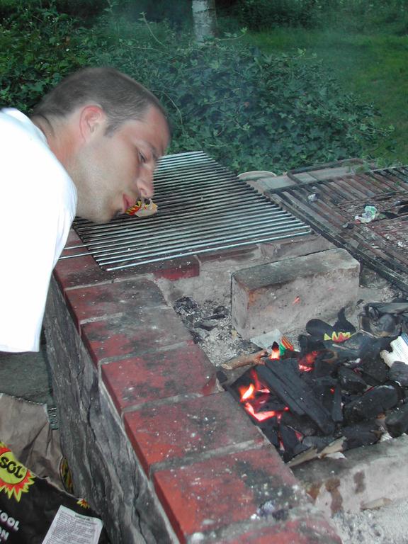 A person in a white shirt blows on a charcoal fire in a brick barbecue to help it ignite.