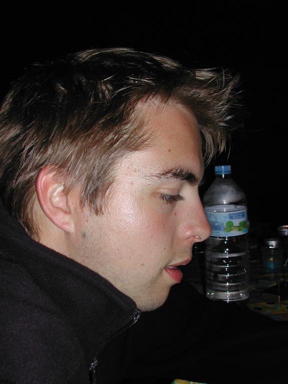 A person in a black jacket sits at a table with a water bottle nearby, looking downward.