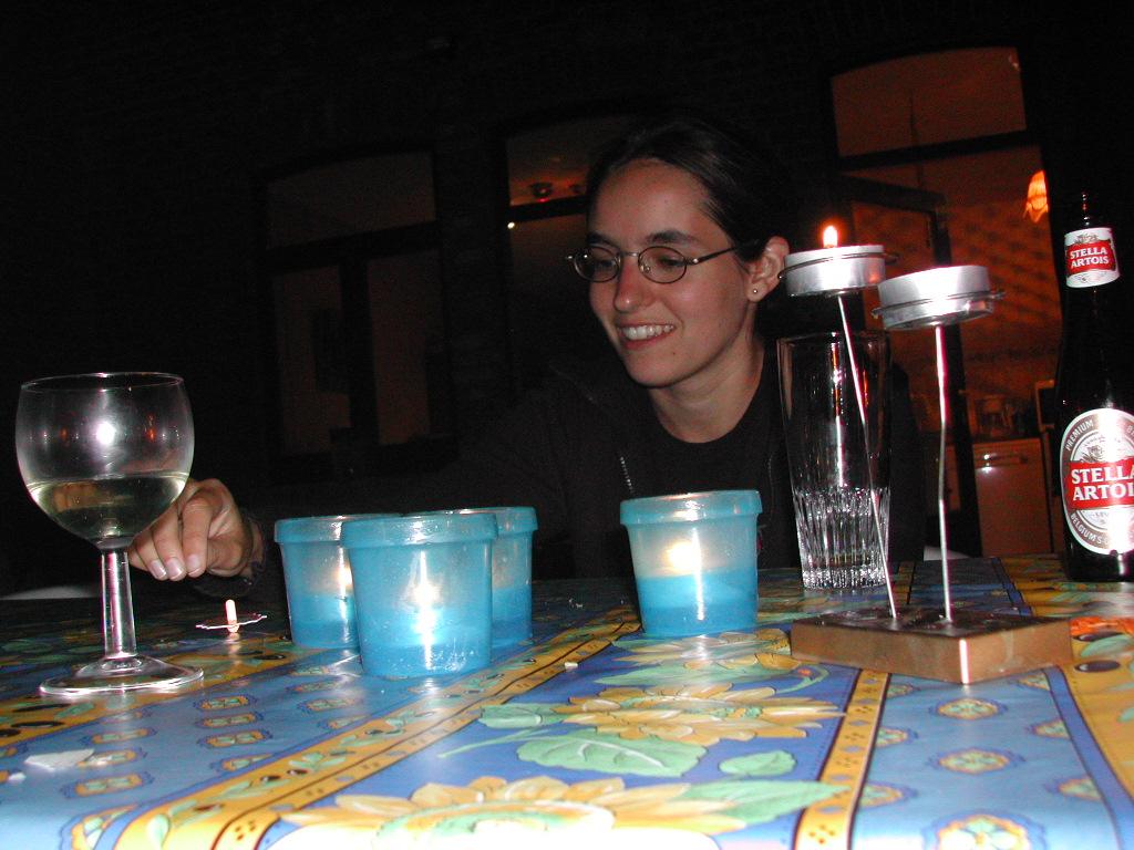 A person smiles while sitting at a table with candles, a glass of wine, and a beer bottle.