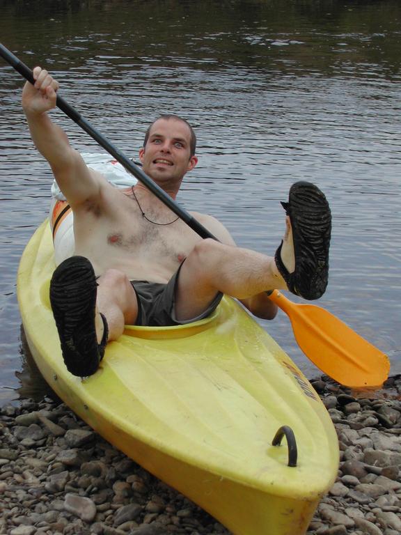 A man sits in a yellow kayak near the shore, holding a paddle and lifting his feet.