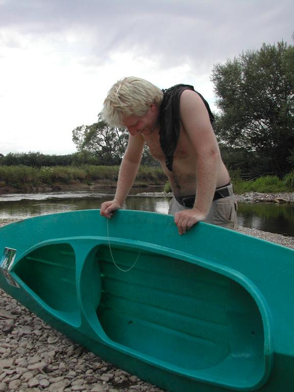 A person looks down at an overturned green kayak on a rocky riverbank.