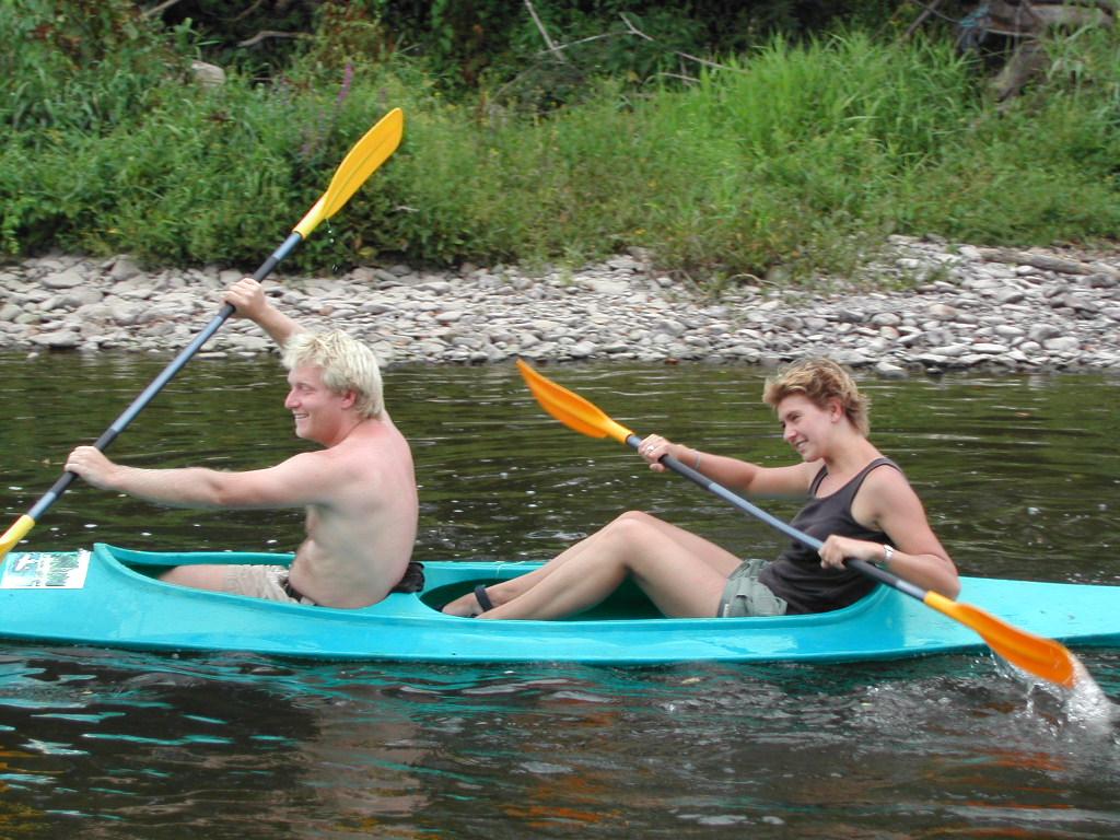 Two people paddling a blue kayak on a river, smiling and looking engaged in the activity.