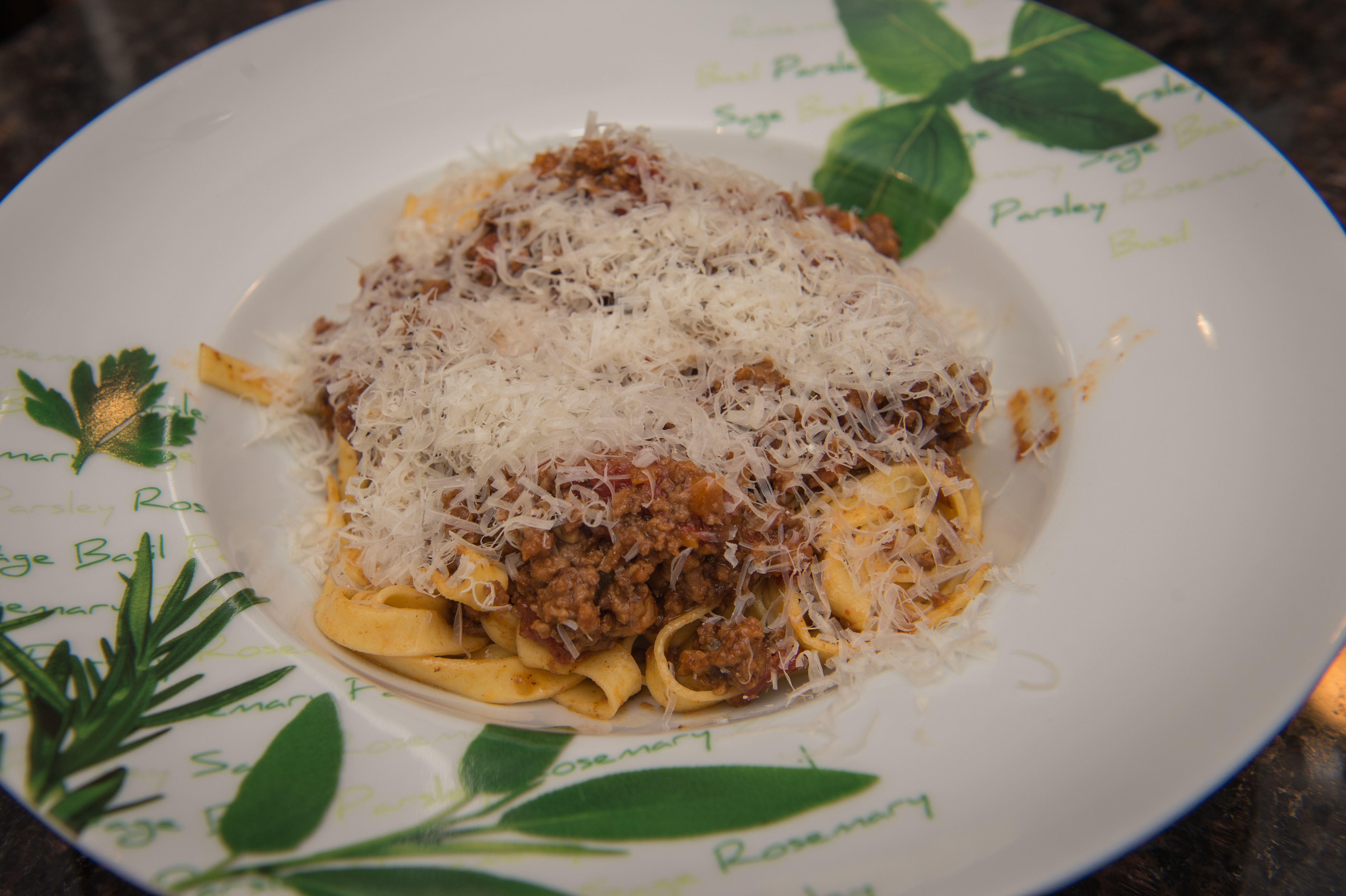 A plate of pasta with meat sauce, topped with grated cheese, served on a decorative dish.