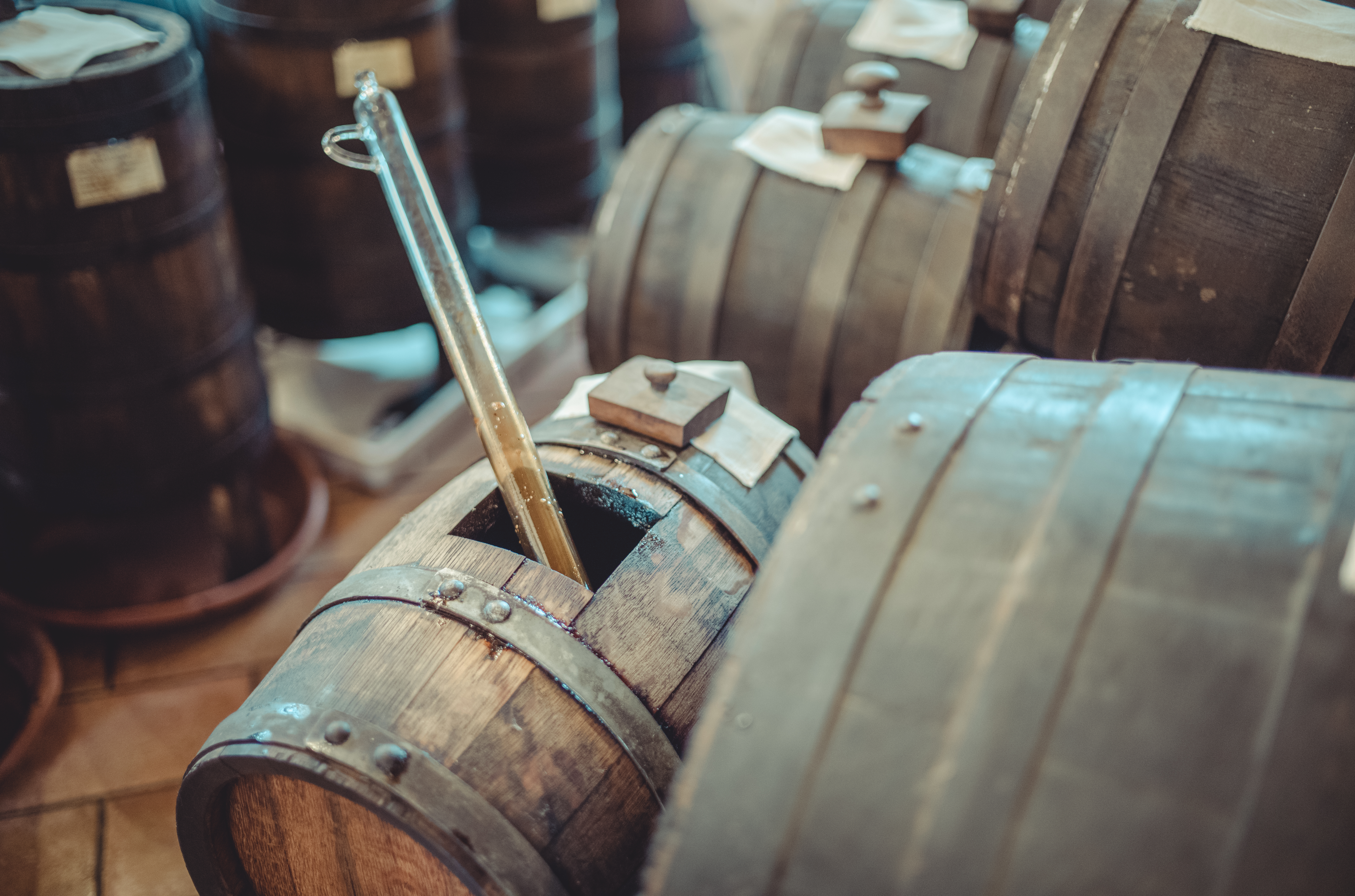 A wooden barrel containing 100-year-old balsamic vinegar with a glass siphon tube partially submerged inside.