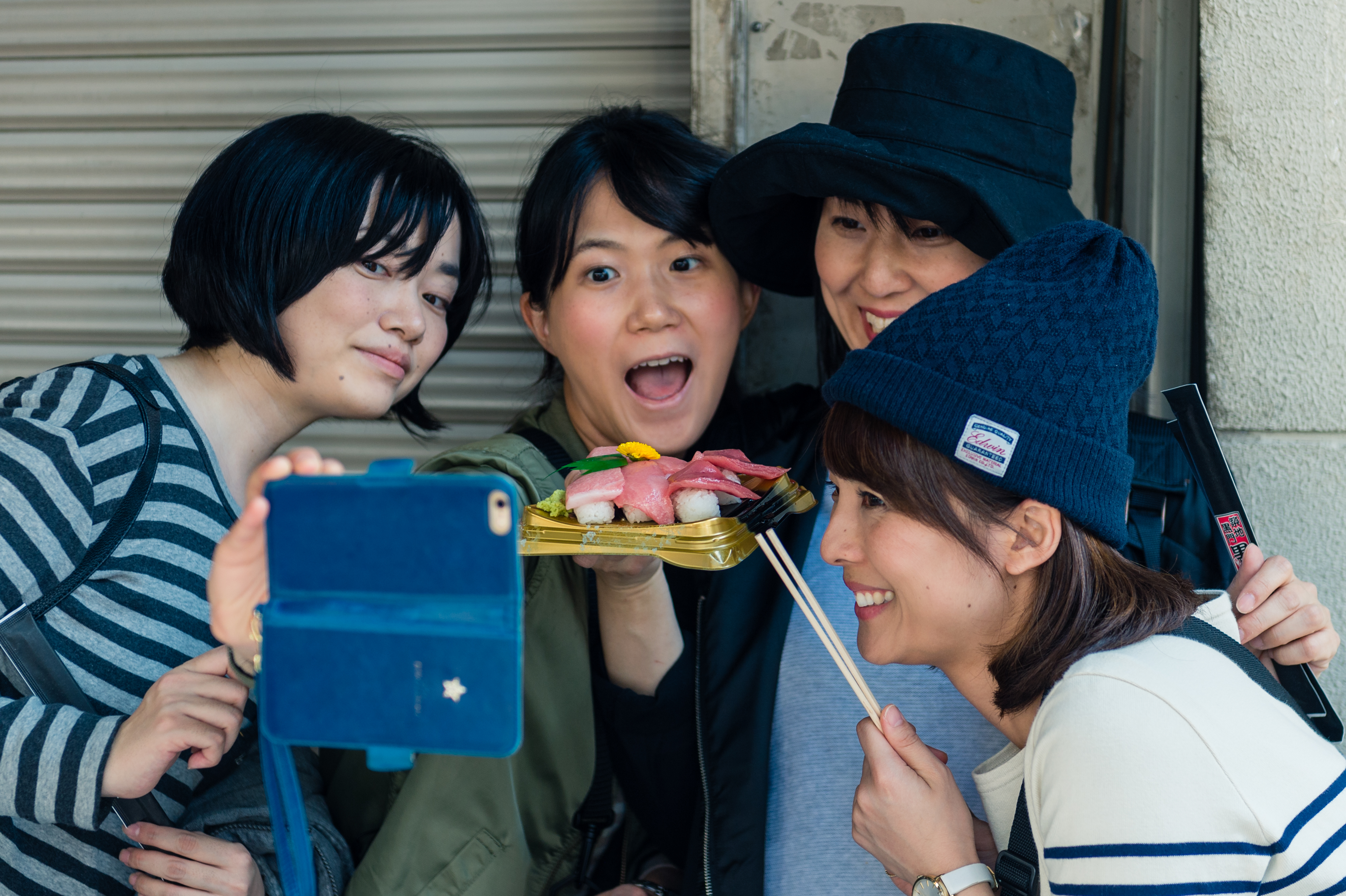 Four friends take a selfie while holding a tray of sushi, smiling and posing together.