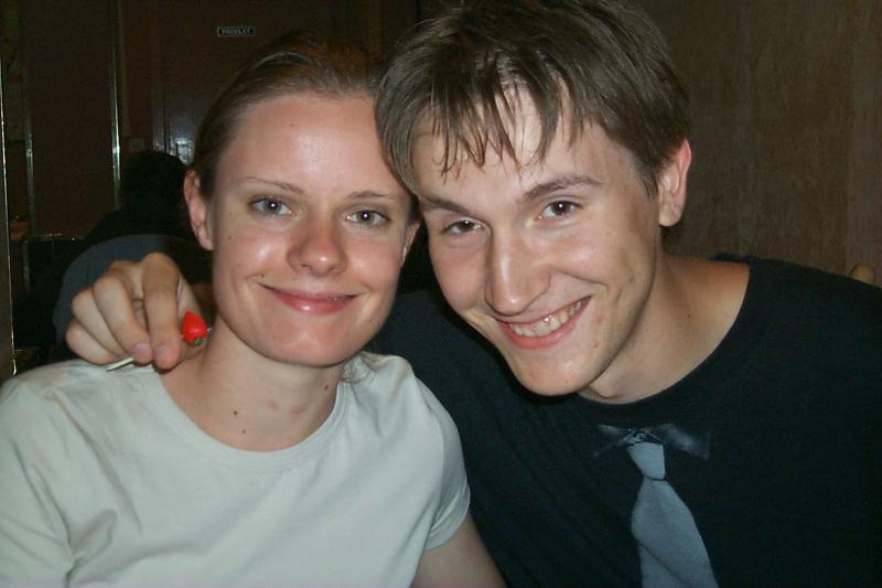 A smiling man and woman sit closely together, with the man's arm around the woman's shoulder.