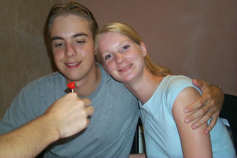 A smiling couple sits together, with one person holding a small red object in front of them.