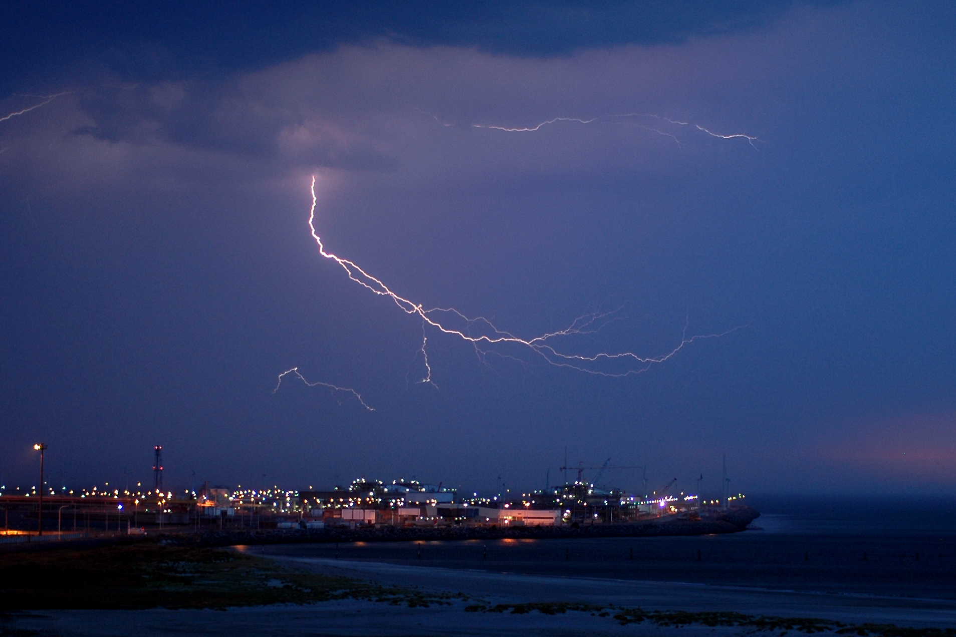 Lightning bolts flash across the dark sky above a brightly lit gas terminal at the Port of Zeebrugge.