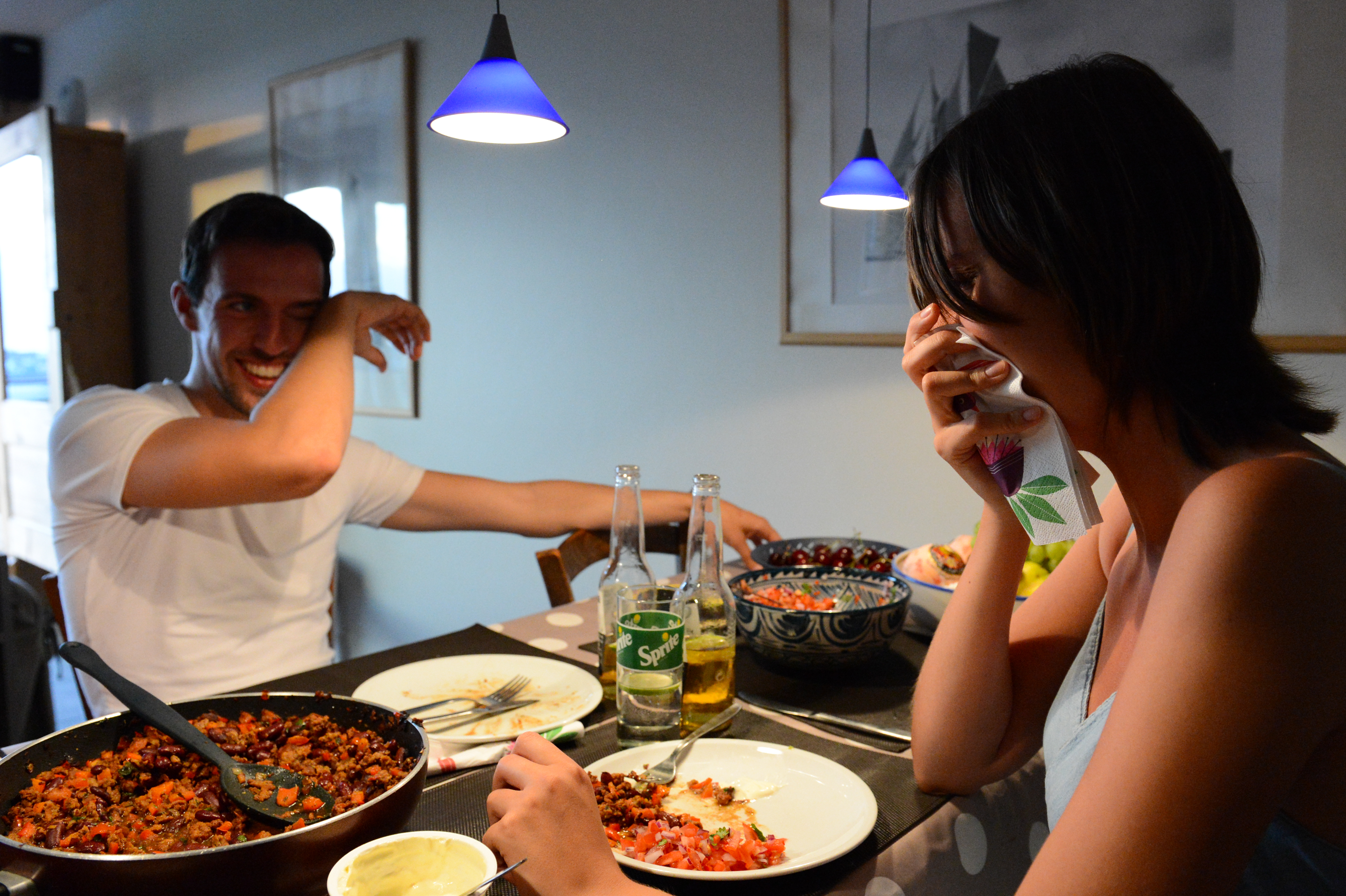 Two people laughing at a dinner table with Mexican food, drinks, and plates in front of them.