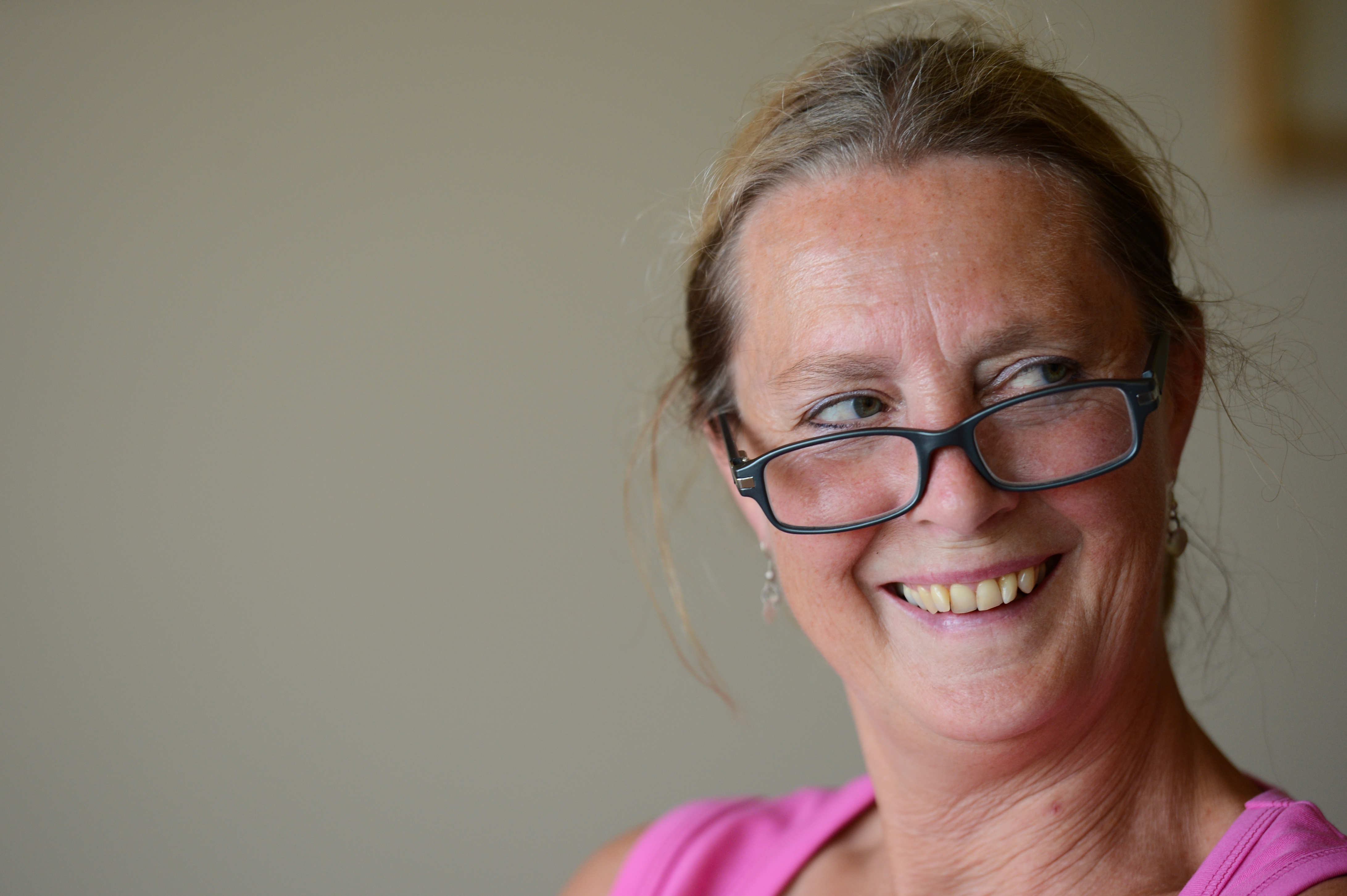 A woman in a pink top smiles while wearing glasses slightly lowered on her nose.