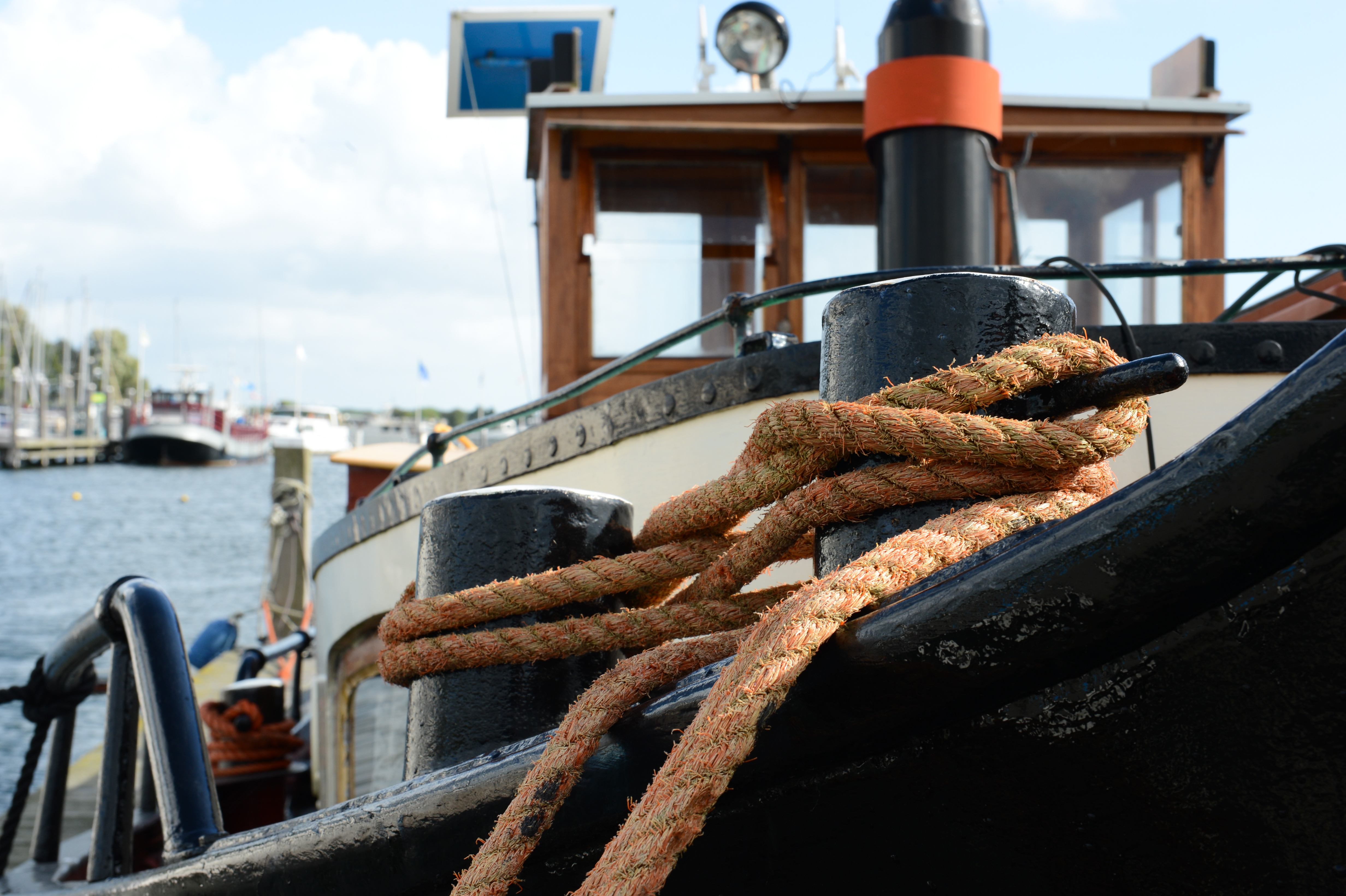 A thick rope is tightly wrapped around a metal post on the bow of a boat in a harbor.