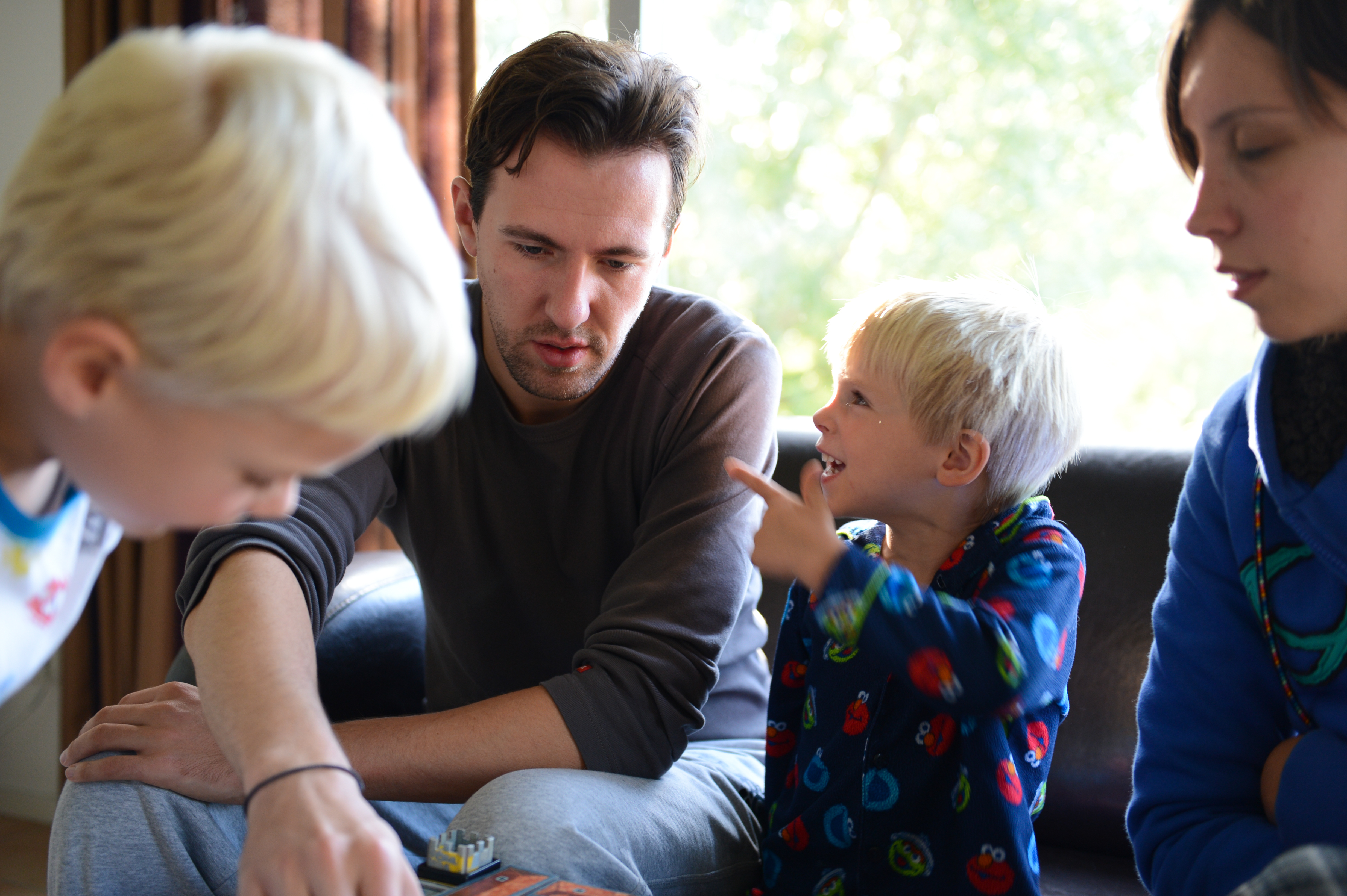 A young child excitedly talks and gestures to a man, while others focus on an activity at a table.