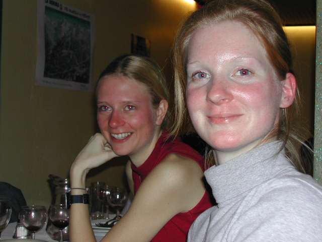 Two women with flushed faces sit at a restaurant table, smiling.
