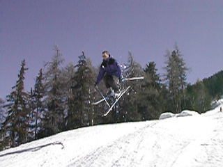 A skier in a purple jacket jumps in the air on a snowy slope.