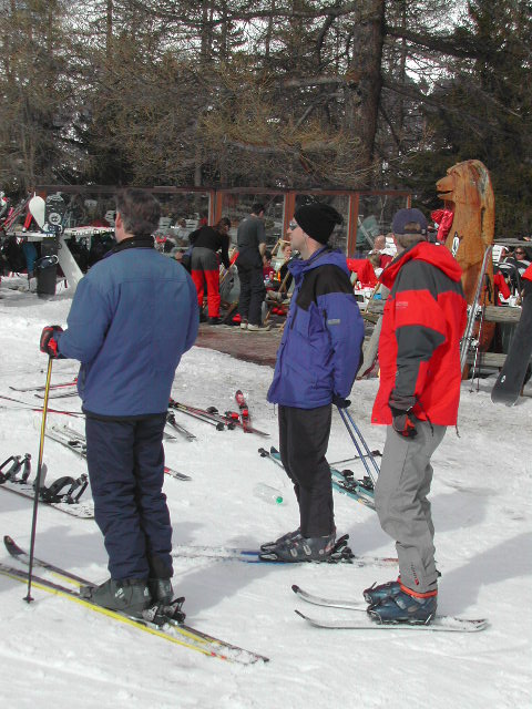 Three people in ski gear stand on the snow with skis, looking ahead.