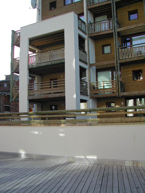 A wooden apartment building with balconies and a white frame structure, viewed from a deck with a railing.