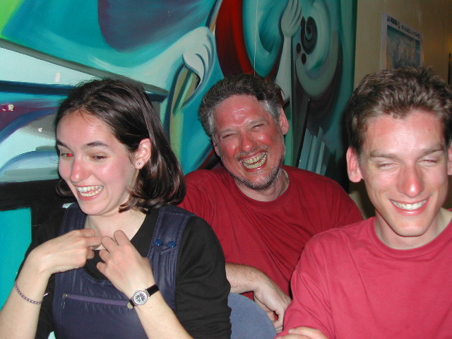 Three people laughing together in a brightly colored room, all appearing joyful and amused.