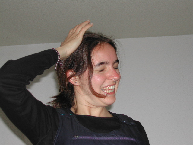 A woman smiles with her eyes closed, touching her head with one hand.