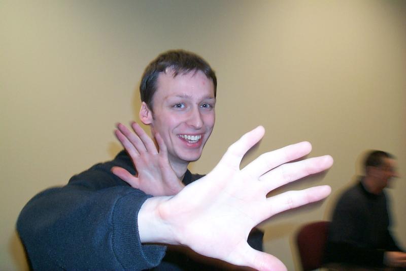 A smiling person in a black sweater playfully holds up their hands toward the camera at a LAN party.