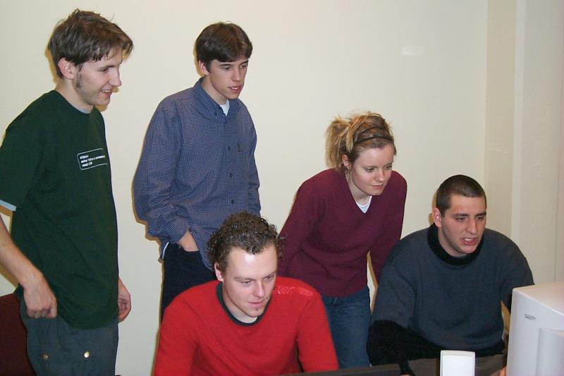 Five young people gathered around a computer, focused on the screen during a LAN party.