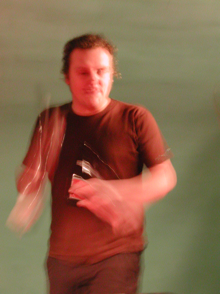 A person in a brown shirt is dancing while holding a drink, with motion blur visible.
