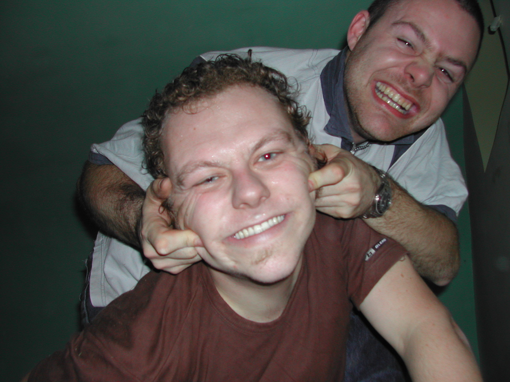 One person playfully pulls another's cheeks while both smile and pose for the camera.