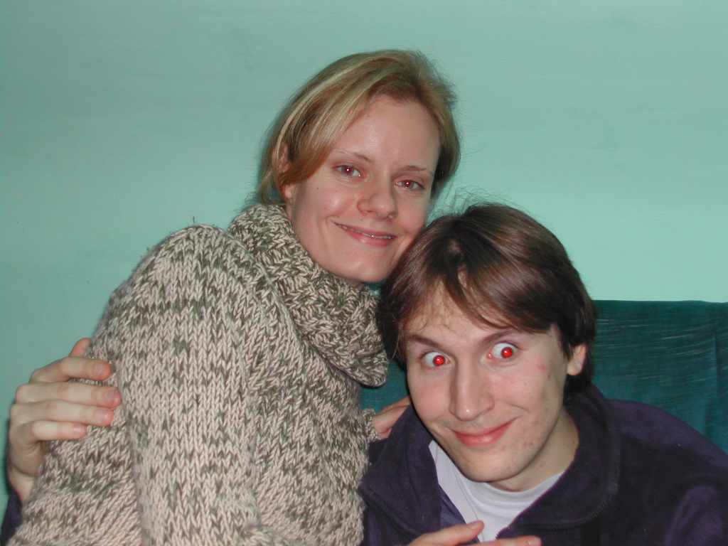 A smiling woman in a knitted sweater sits close to a man, who is also smiling at the camera.