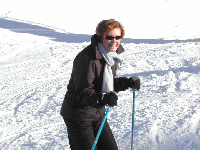 A person wearing a black jacket and scarf smiles while skiing on a snowy slope.