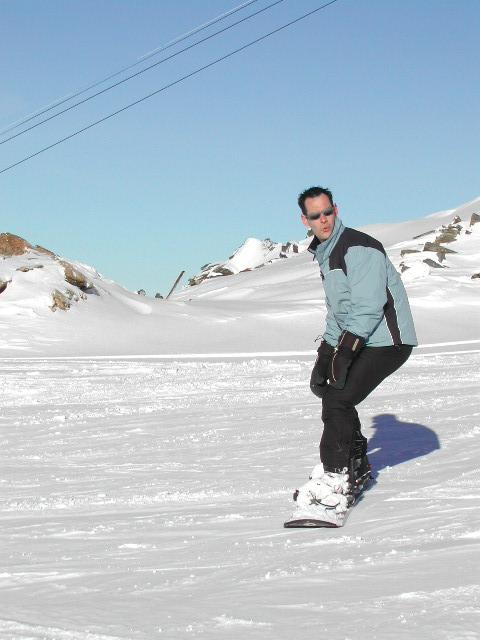 A person wearing a blue and black jacket snowboards on a snowy slope under a clear sky.