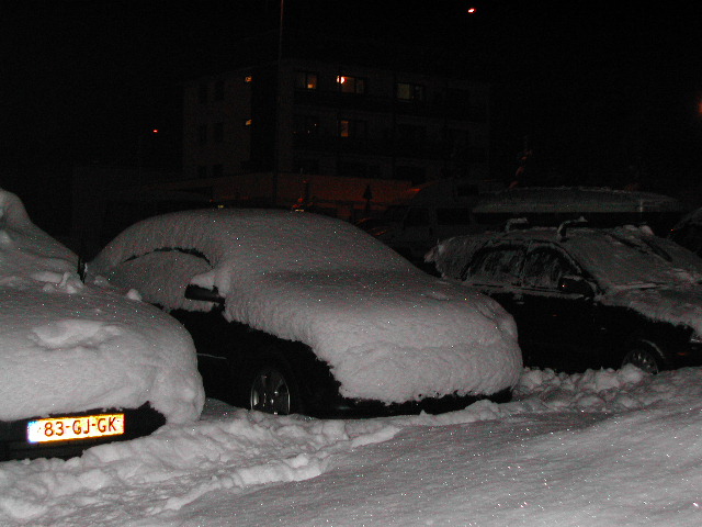 Several cars parked outside at night, covered in a thick layer of snow.