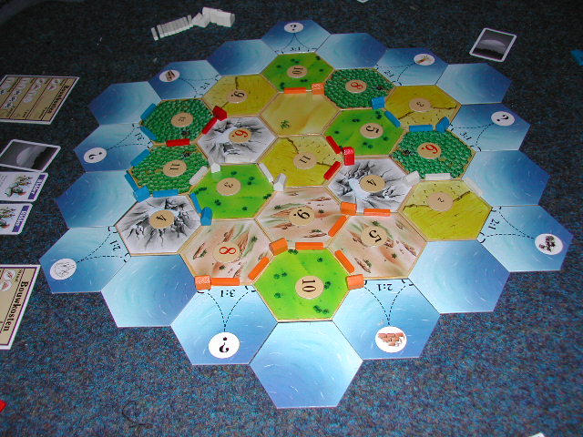 A Settlers of Catan board game is set up on a carpeted floor, with roads and settlements placed.