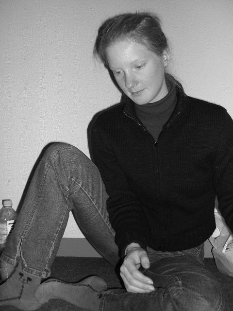 A person sits on the floor, wearing a dark sweater and jeans, looking downward with a neutral expression.