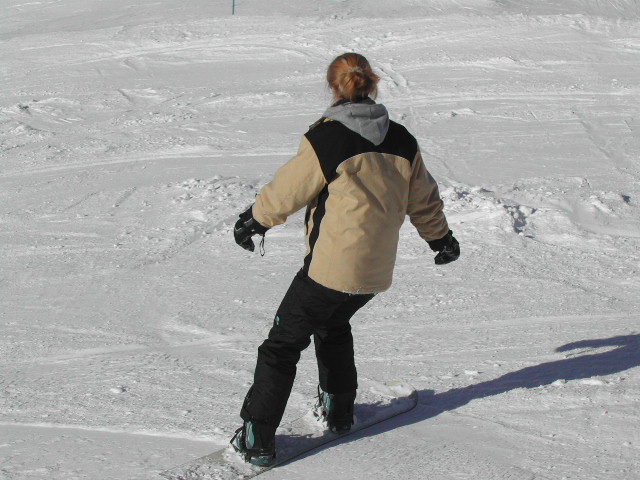 A person snowboarding on a snowy slope, wearing a beige and black jacket with a hood.