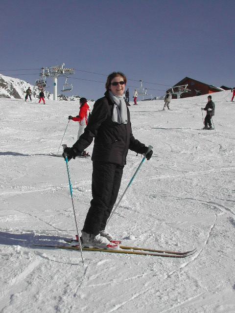 A person in black ski gear stands on a snowy slope, holding ski poles and smiling at the camera.