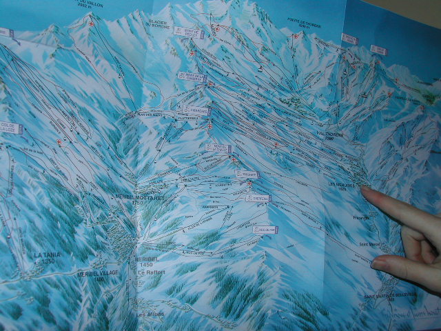 A person points at a ski resort map showing trails and locations in Les Menuires.