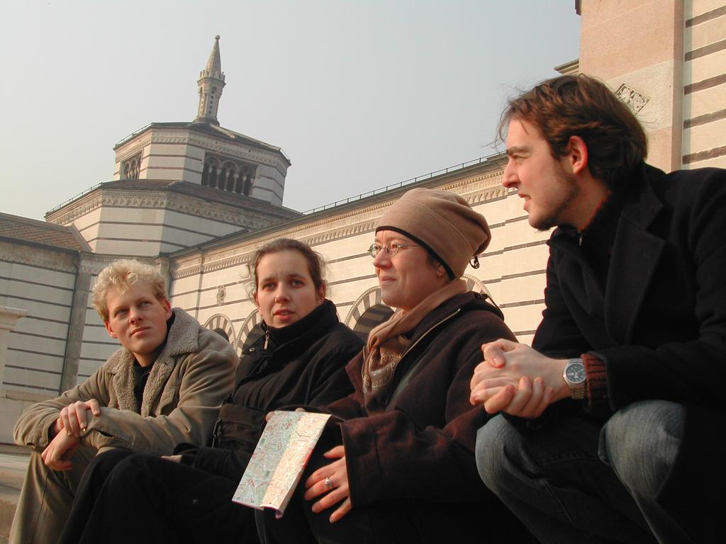 Four people sit on steps outside a historic building, engaged in conversation.