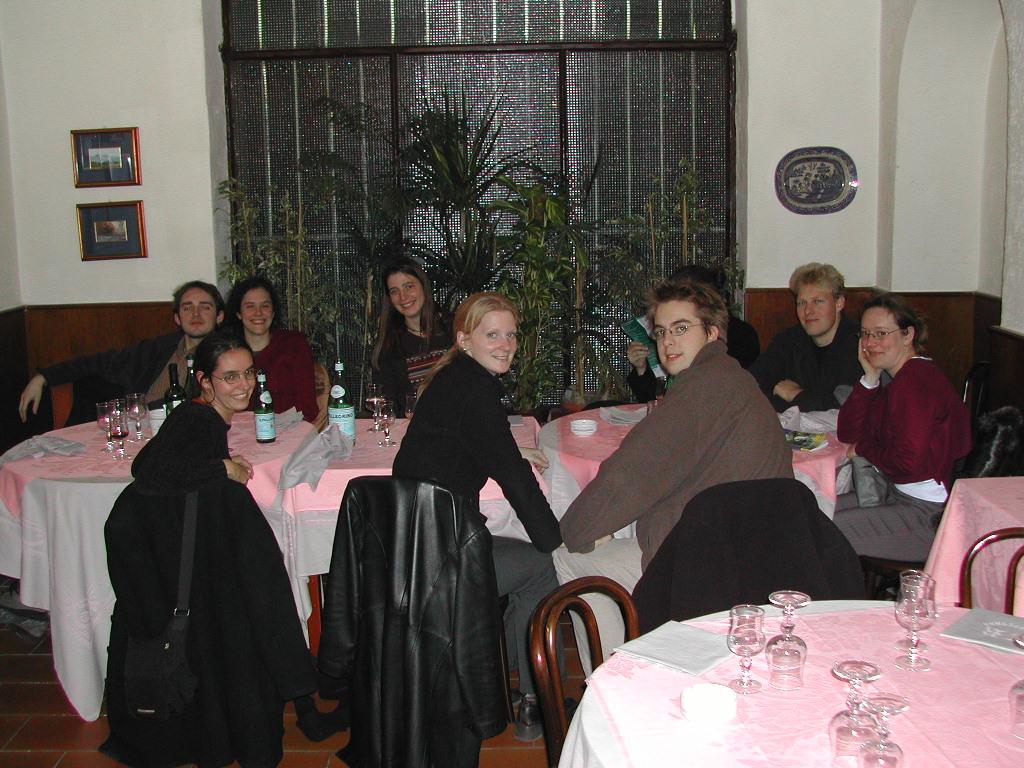 A group of eight people sits at a restaurant table with pink tablecloths, smiling and looking at the camera.