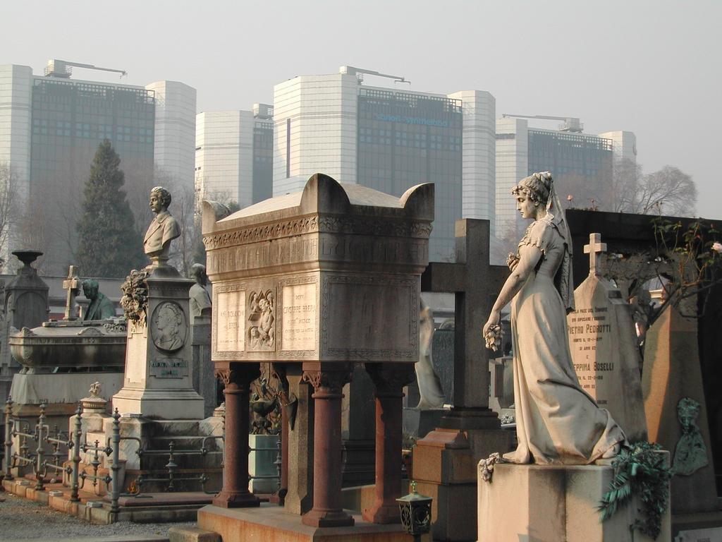 A cemetery with ornate statues and tombs, with modern glass buildings in the background.