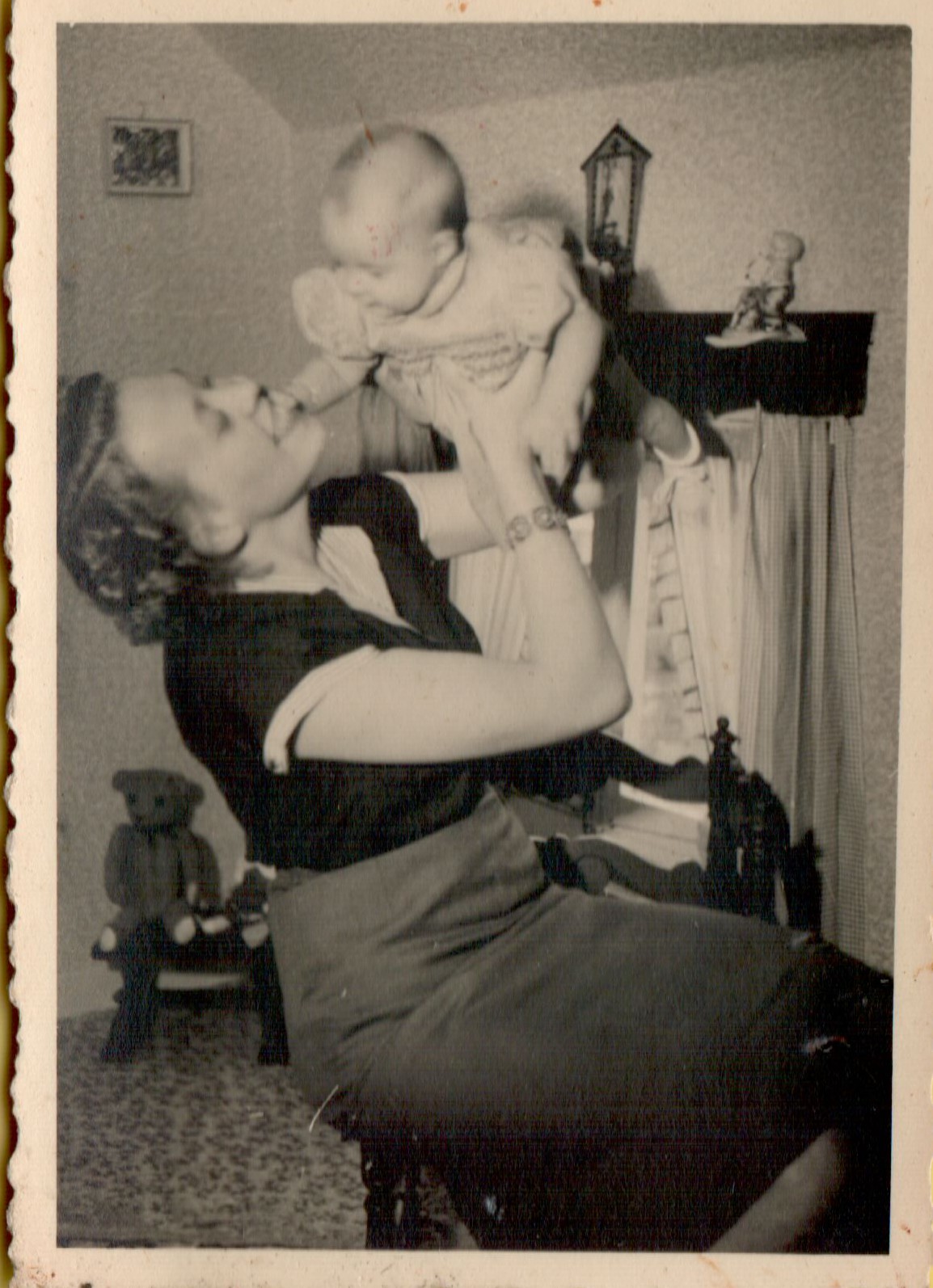 A woman lifts a baby in the air while smiling as the baby reaches for her face.