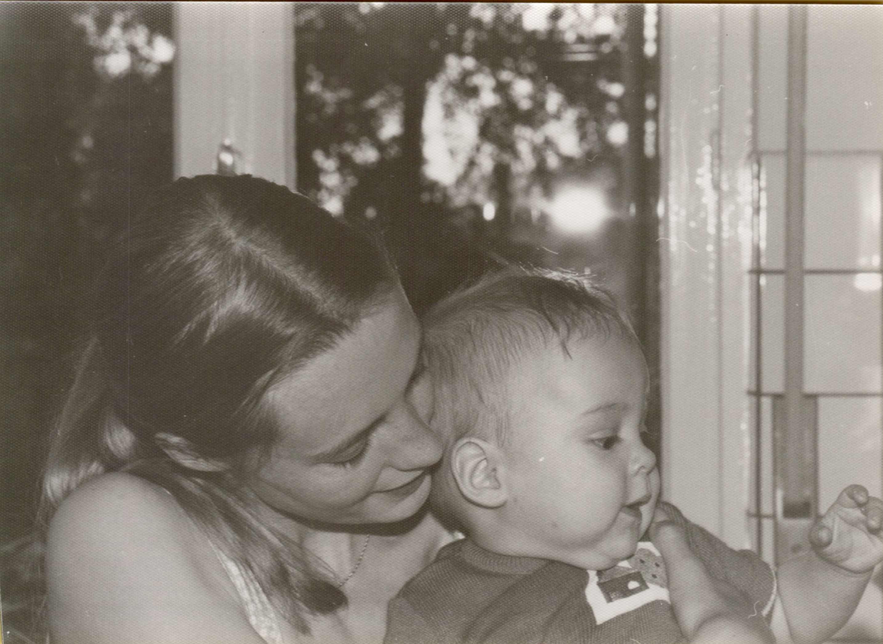 A mother holds her baby close, smiling as she looks at them.