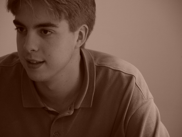 A young man in a polo shirt looks to the side with a neutral expression.
