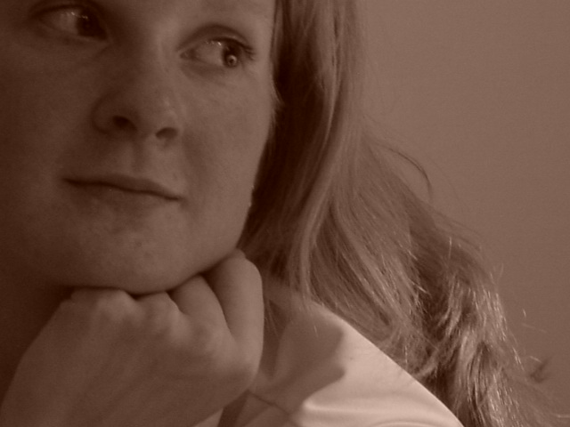 A woman with long hair rests her chin on her hand, gazing to the side with a thoughtful expression.