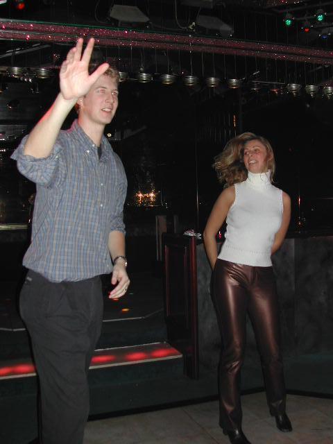 A man raises his hand while dancing, and a woman dances beside him in a dimly lit venue.